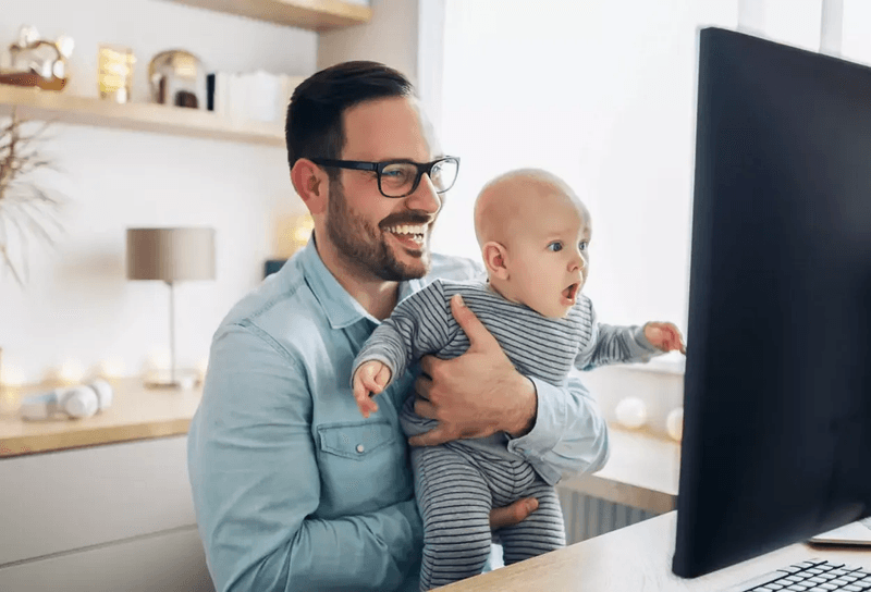 man in glasses holding a baby in front of a computer 